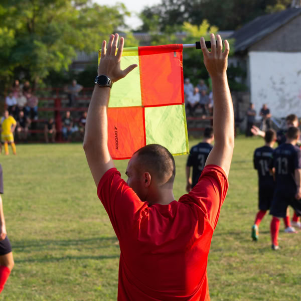 A soccer referee holds up a flag on the field during a game, signaling to players.