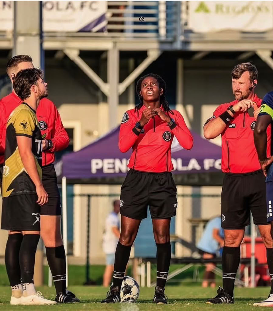 Referee issuing a red card to a soccer player in an outdoor match setting.